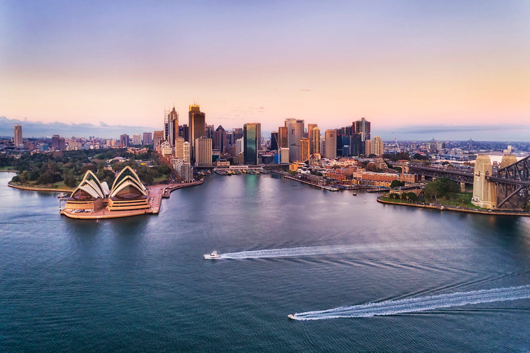 Sydney harbour and skyline captured at sunset with two boats zipping across the water
