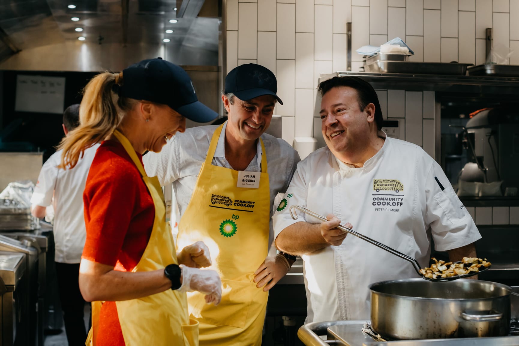 Three people standing in a kitchen, laughing over a huge pot of food.