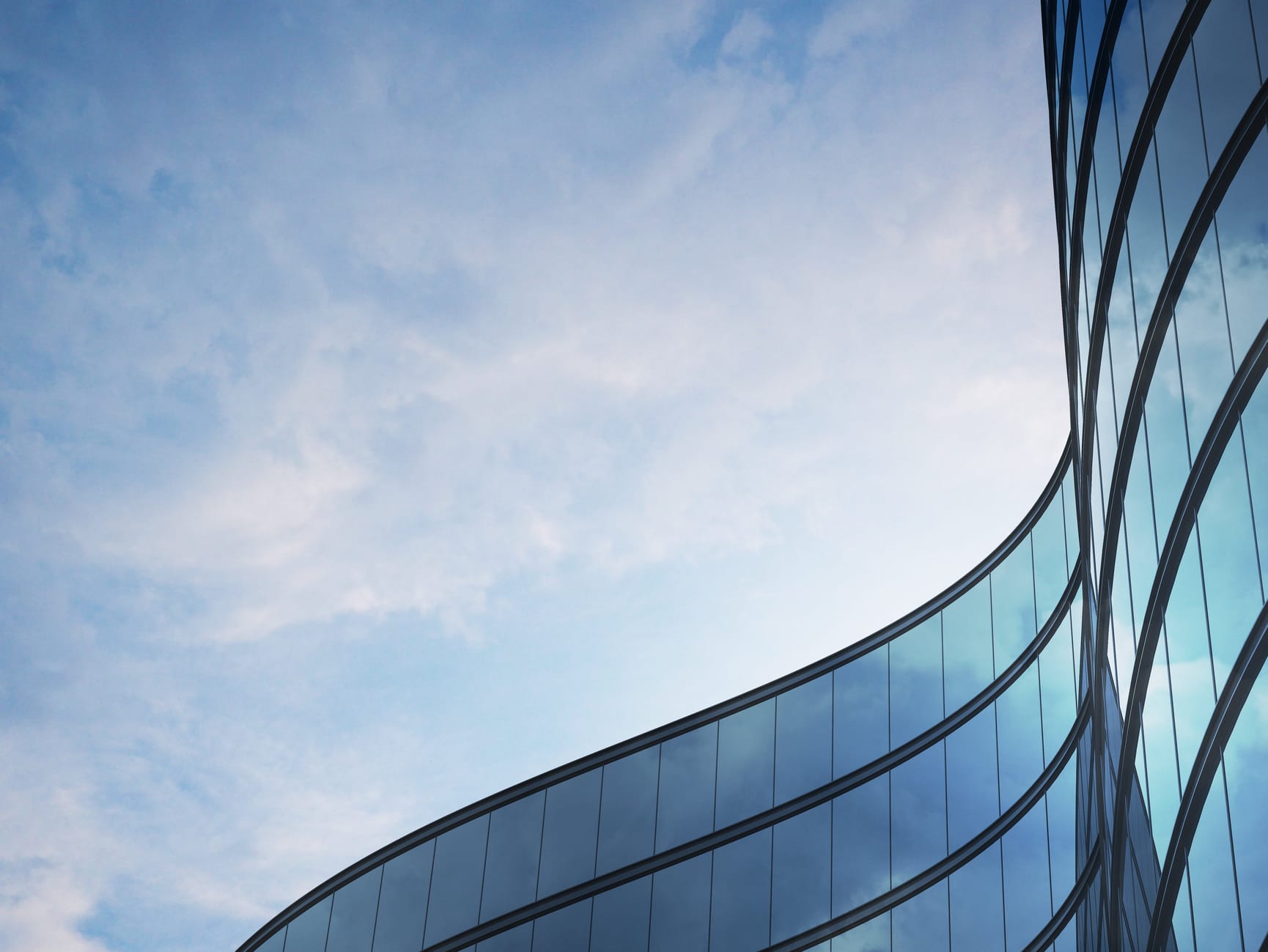 Seen from the low angle of a glass office building with wave wall form, in front of a slightly cloudy sky,.