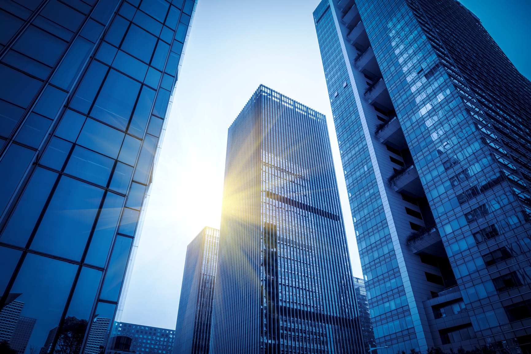 View looking up at four glass skyscrapers with sunlight streaming from behind centre buildings.